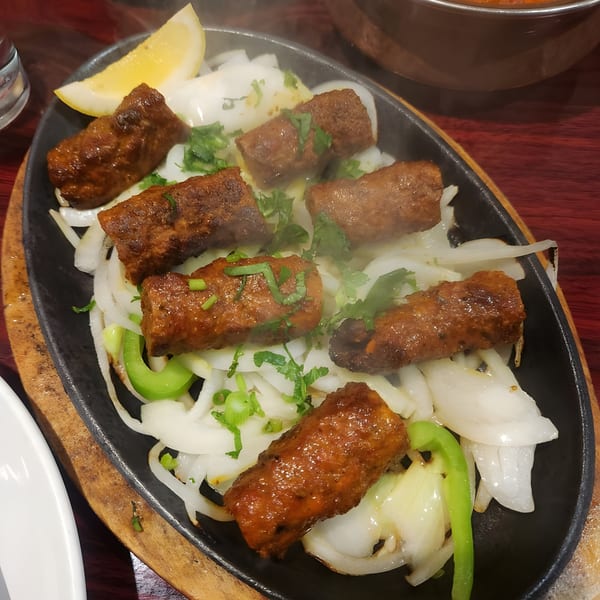Sizzling Indian seekh kebabs with onions, green peppers, and cilantro on a hot plate.