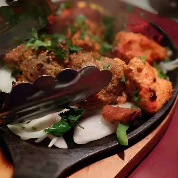 Sizzling Indian chicken tikka and kebabs with onions and cilantro on a hot plate.
