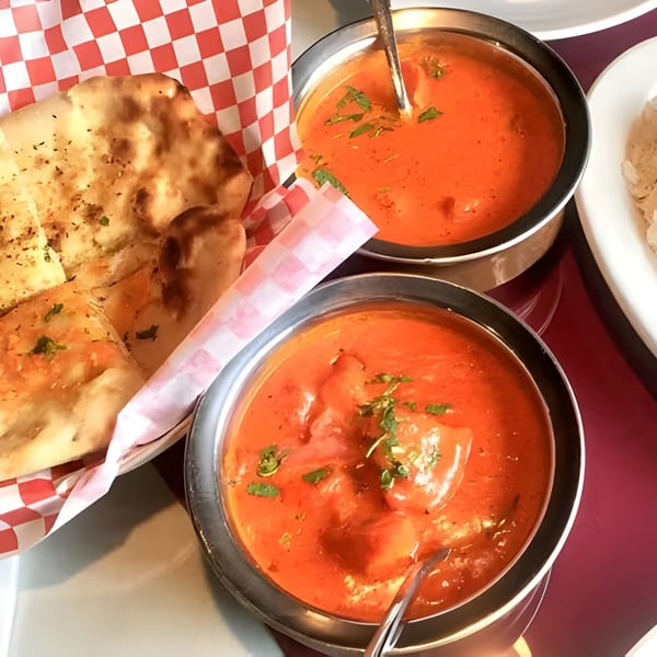 Two bowls of Royal Everest Indian butter chicken with naan bread in a checkered basket.