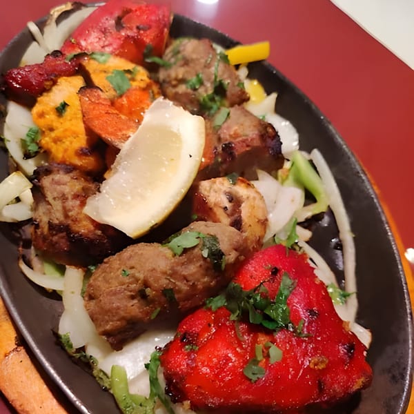 A Royal Everest Indian mixed grill platter with various meats, onions, and a lemon wedge.