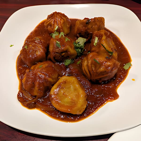 Royal Everest's Indian momos, steamed dumplings in a rich, spicy red sauce, garnished with fresh cilantro.