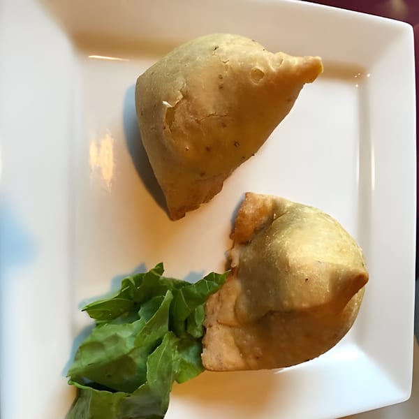 Two golden-brown samosas and a small pile of fresh green lettuce on a white square plate.