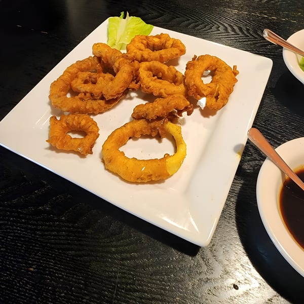 A white rectangular plate filled with golden-brown fried onion rings and a side of lettuce.